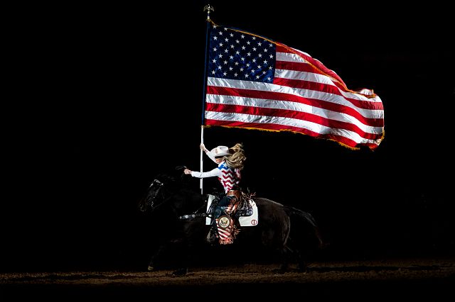 A woman riding a horse while holding an american flag.