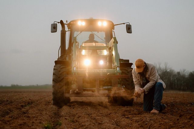 A man wearing Justin Boots kneeling in front of a tractor