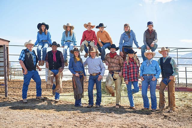 A gorup of men and women wearing western gear posing for the camera.