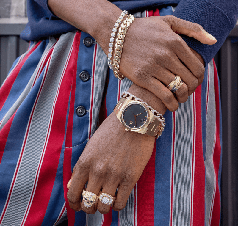 A man clasps his hand over his other wrist, revealing stunning bracelets, rings and a watch