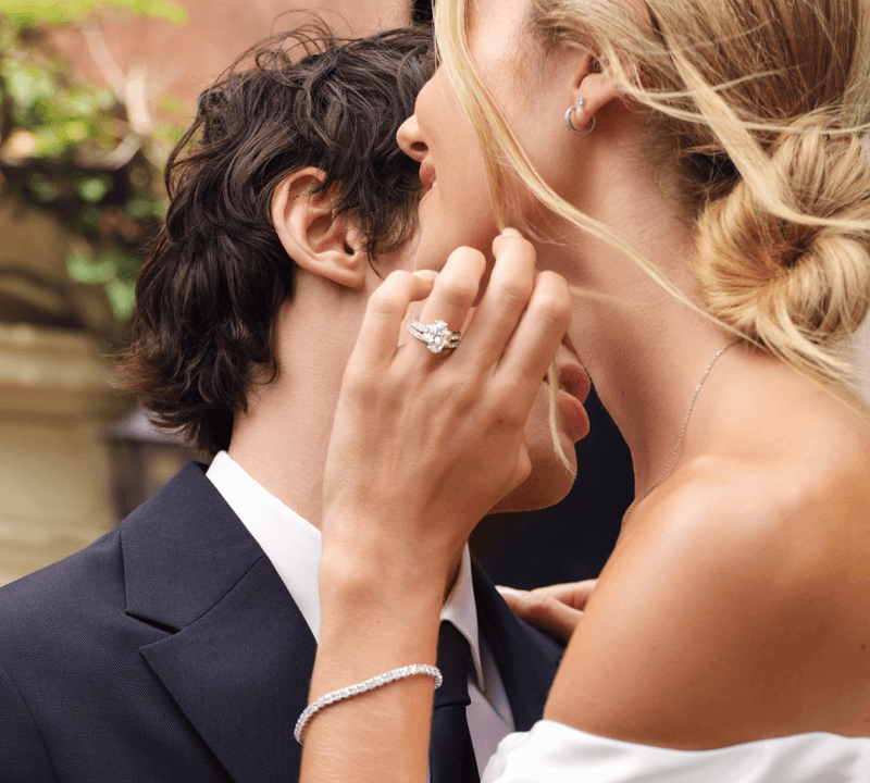 Bride and groom embraces, while bride showcases bracelet, ring, earrings and necklace.