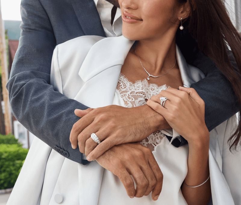 Couple embraces showcasing earrings, necklace, bracelet and rings.