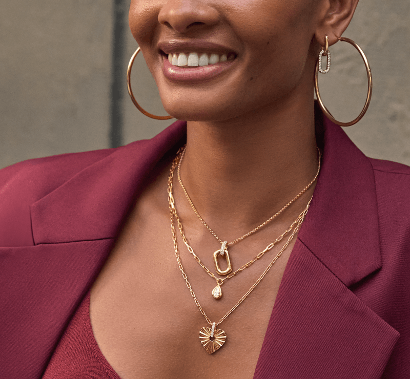 Woman showcasing gold hoop earrings and layered necklaces.