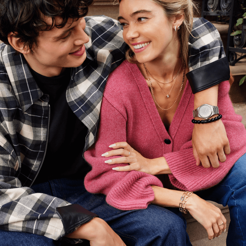 Man embracing woman showcasing watch, bracelets, necklaces, rings and earrings