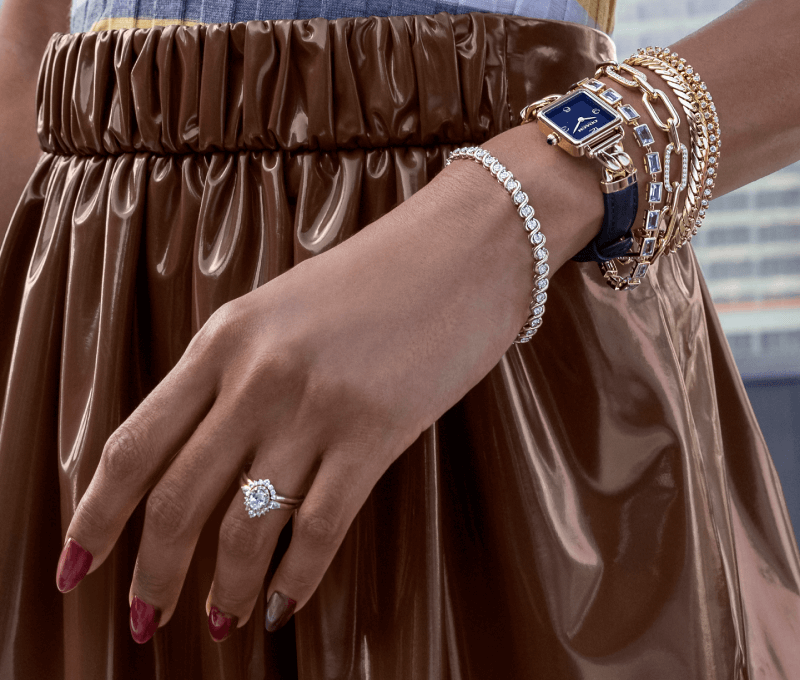 Woman wearing a brown skirt showcasing a stack of bracelets, watch and ring.
