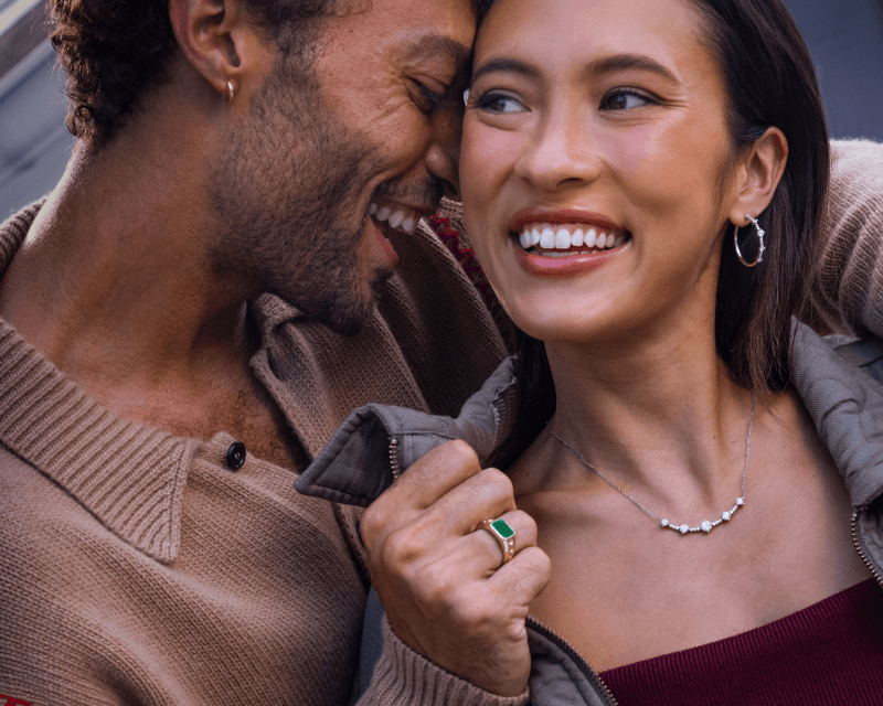 A smiling couple poses, adorned with beautiful Diamond Jewelry.