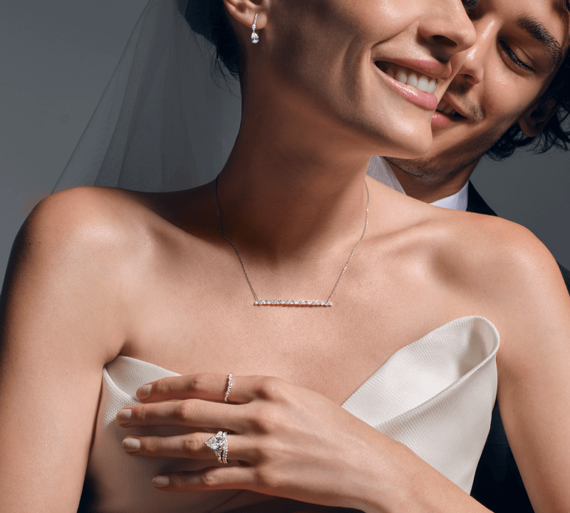 Image showcasing a bride displaying stunning bridal jewelry set. Diamond Earrings, a Bar Necklace, and two Diamond Rings