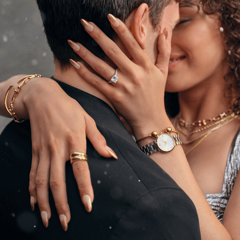 A woman embraces a man, showcasing stunning watch, bracelets, rings and necklaces.