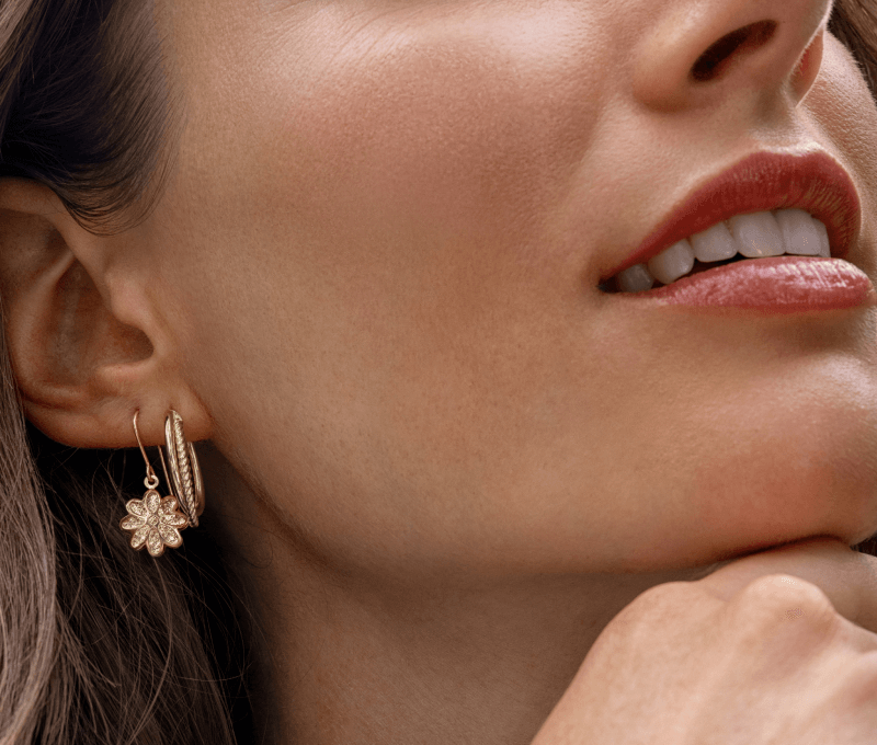 Image showcasing a woman wearing stunning gold earrings, featuring a hoop and floral charm design.