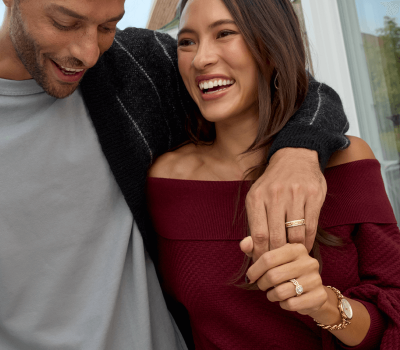 A couple poses wearing elegant jewelry, including wedding bands, and a stylish wristwatch.