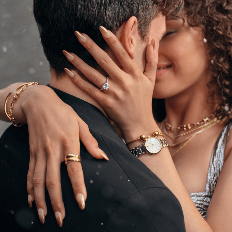 Image of an embracing couple showcasing a stunning Diamond Engagement Ring paired with Gold Jewelry – including layered Necklaces, Bracelets, and a Watch.