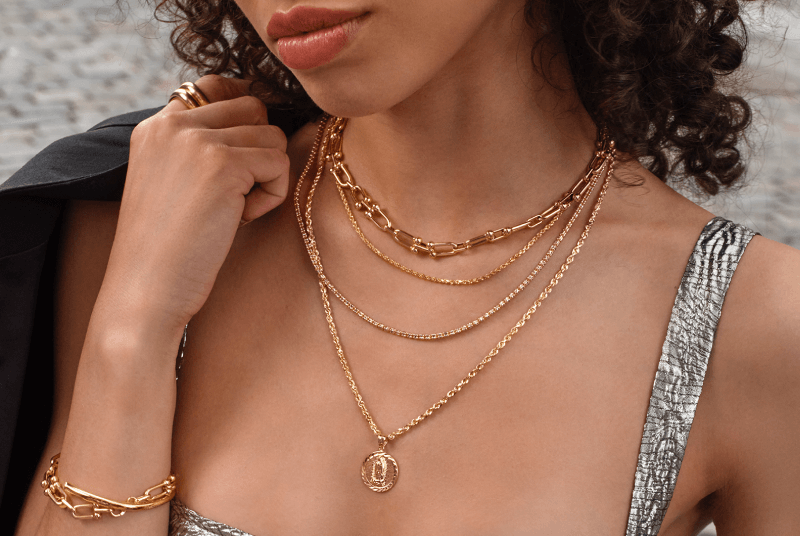 Image showcasing a woman showcasing layered Gold Necklaces with a pendant, paired with a Gold Bracelet and Ring.