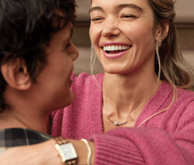 Smiling couple, woman wearing a variety of fine jewelry including earrings, necklace, bracelet and watch.