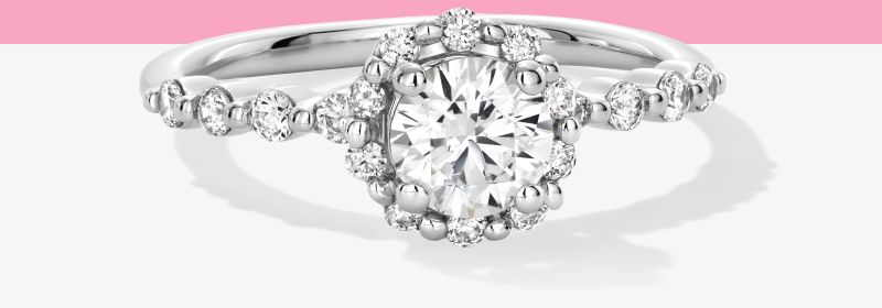 Round cut diamond engagement ring with a halo of smaller diamonds and a pavé set band in white gold.