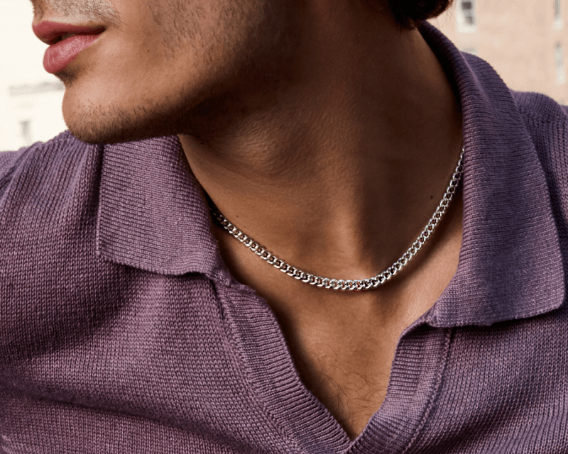 Model wearing a silver curb chain necklace, shown close up at neckline with textured knit shirt.