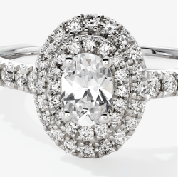 White gold engagement ring with an oval diamond center and double pavé diamond halo and band.