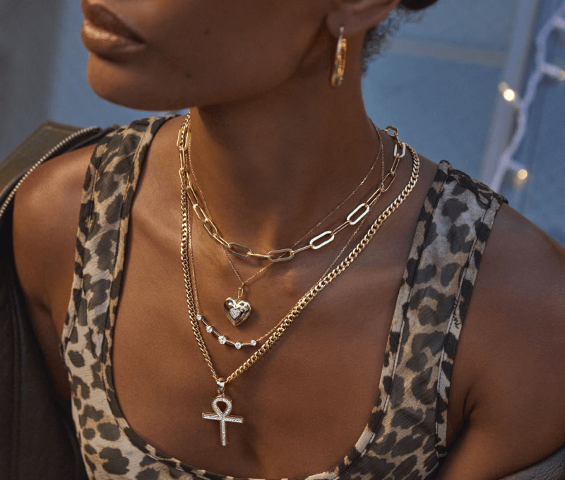 Woman in leopard top wearing yellow gold layered necklaces and yellow gold hoop earrings.