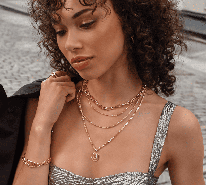 Model Wearing Layered Gold Necklaces With Coin Pendant, Chain Bracelet, and Gold Ring.