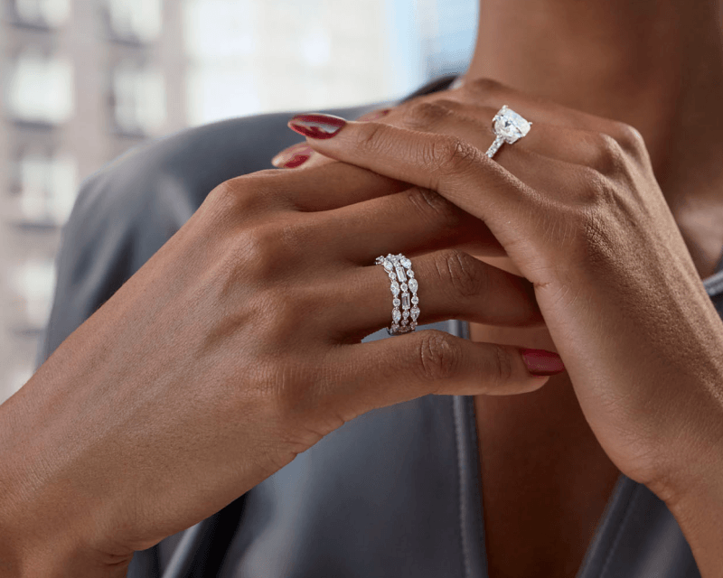 Woman wearing white gold diamond emerald-cut engagement ring and trio of white gold diamond rings.