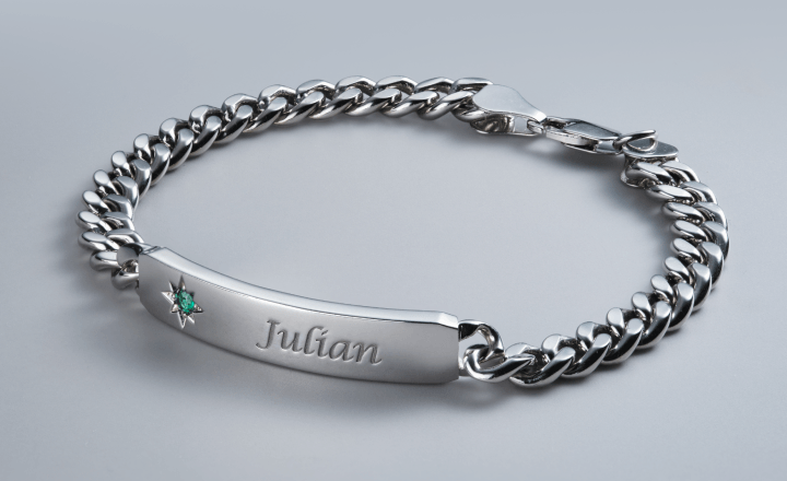 Engraved silver ID bracelet with chain link design and emerald gemstone.