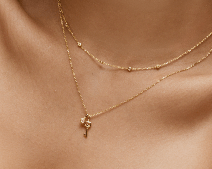 Close-up of layered yellow gold necklaces with key charm pendant and bezel-set diamond accents on neckline.