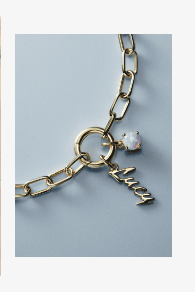 Yellow gold paperclip chain bracelet with script letter charm and opal gemstone accent.