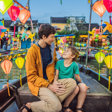 A man and a young boy smiling at each other in a boat decorated with colorful lanterns.