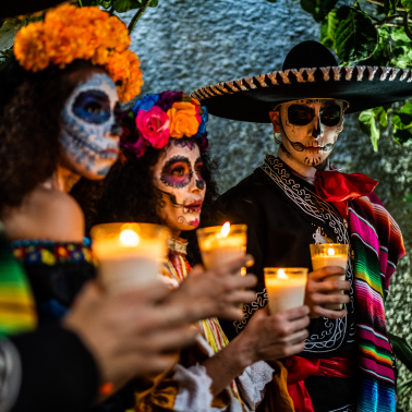 Three people in Halloween costumes with sugar skull makeup, holding lit candles.