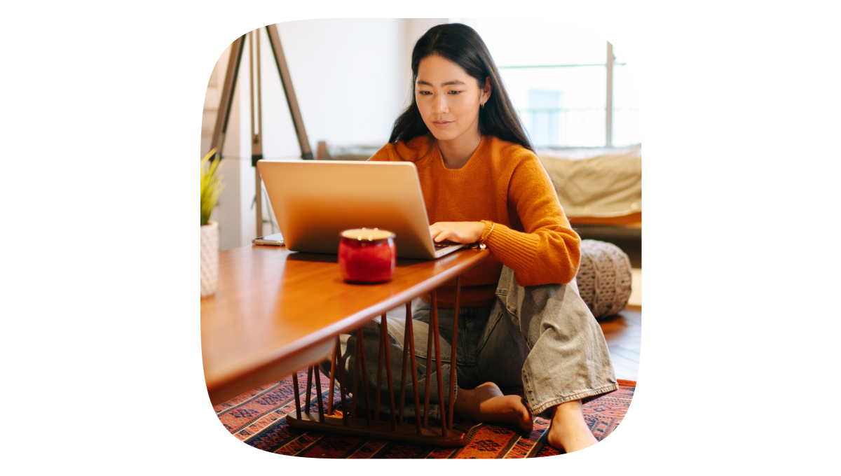 A young woman wearing an orange top, sitting at her laptop and searching.