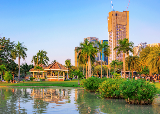 A tranquil park in Bangkok with a traditional pavilion, a pond, and a modern skyline.