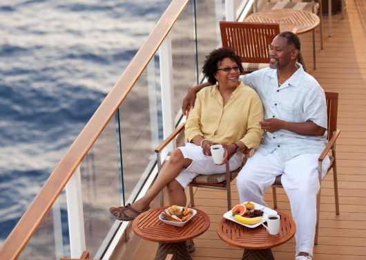 An older couple smiling and relaxing on a cruise ship balcony.