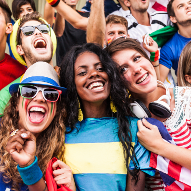 Three smiling young people, possibly fans at a sporting event, celebrating in a crowd.