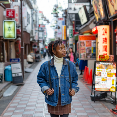 A person wearing a denim jacket and backpack walking down a busy street lined with shops and signs.