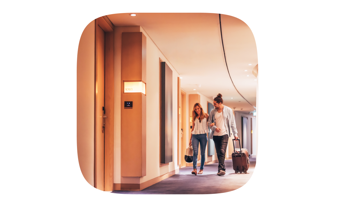 A couple is walking and smiling through the hotel corridor, holding hands.