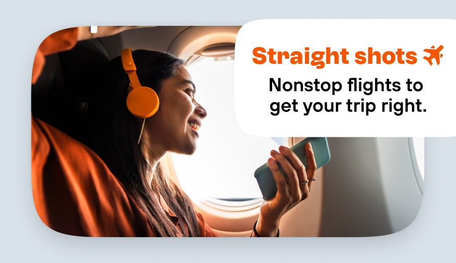 Woman wearing orange headphones smiling at an airplane window.