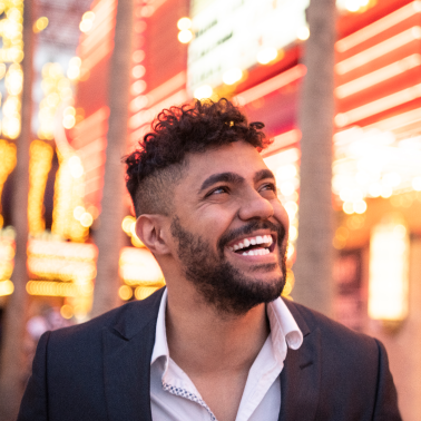 Smiling man in a suit under bright city lights, looking up.