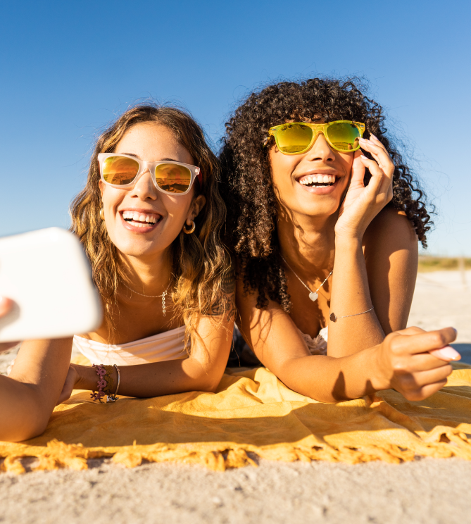 Two friends smiling and taking a selfie on the beach.
