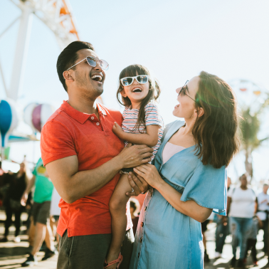 Parents holding a smiling child wearing sunglasses.