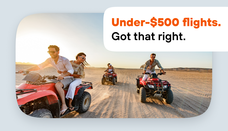 Group riding red ATVs across a sandy desert at sunset.