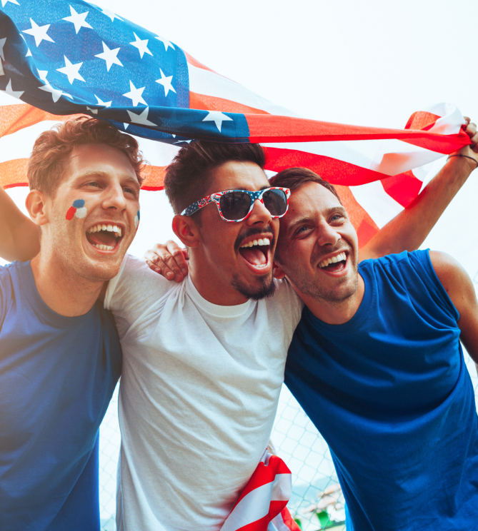 Three friends cheering under a waving American flag.