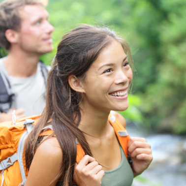 Smiling woman with a backpack hiking in a green forest.