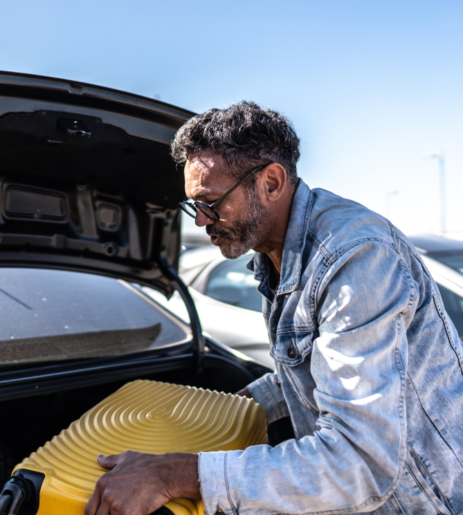 Man lifting a yellow suitcase into a car trunk.