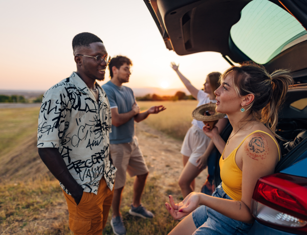 Friends chatting and relaxing at the open trunk of a car at sunset.