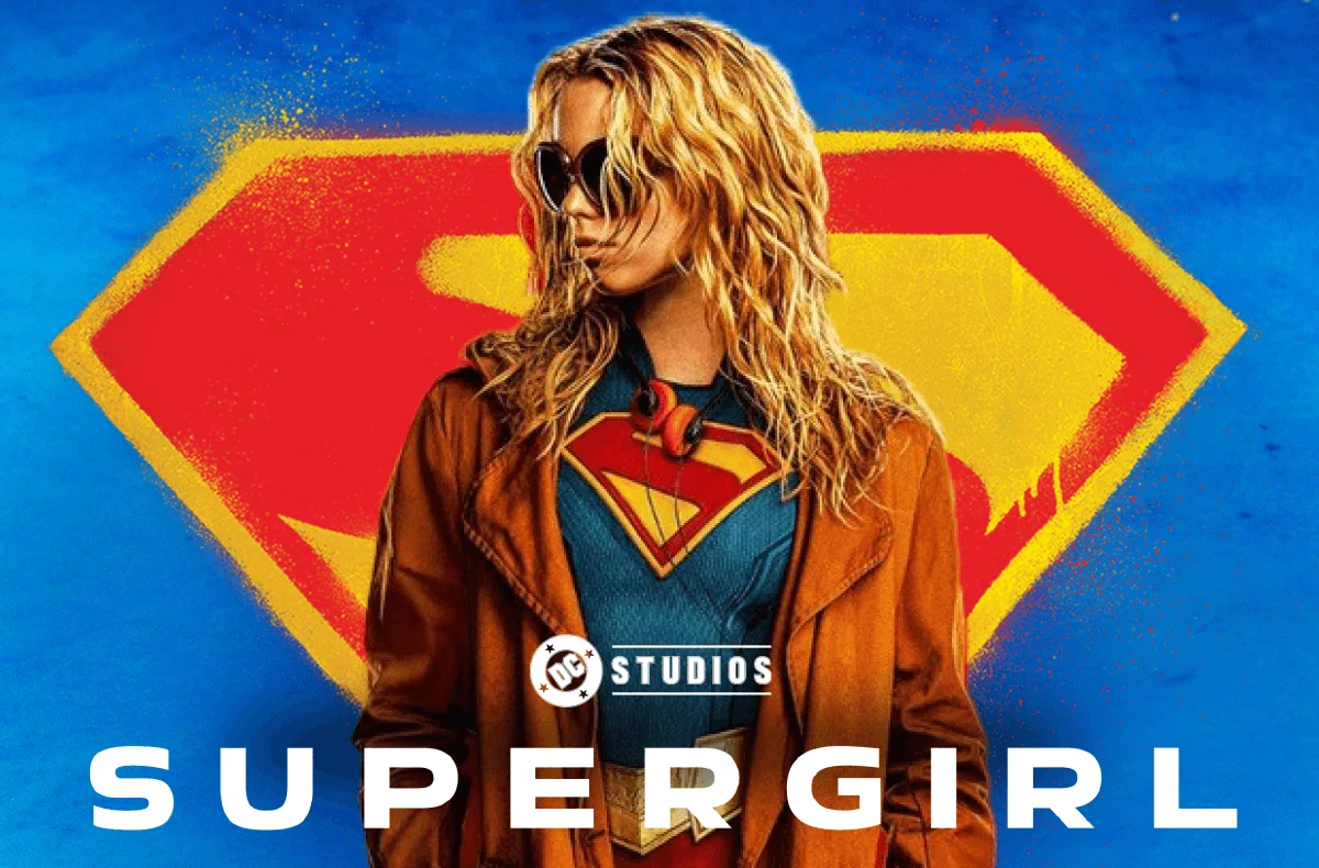 Supergirl in a leather jacket and sunglasses standing infront of the Superman S looking to the left