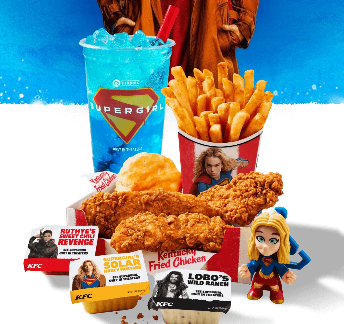 KFC Chicken in a box with a biscuit. Fries and a drink are positioned behind the box. In front of the box are three different Supergirl inspired sauces and a collectable Supergirl plastic doll.