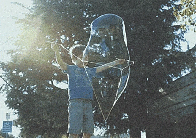 (GIF showing a child making a huge bubble with the wand outdoors)