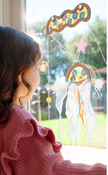 Ocean Quest from Koala Crate. Image of young girl playing with colorful jellyfish that suctions to any window. Pull the strings to make the jellyfish go up, down, and wiggle all around!