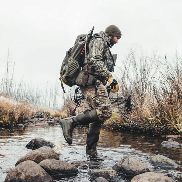 Man wearing Alphaburly Aero in Major Brown crossing a rocky creek