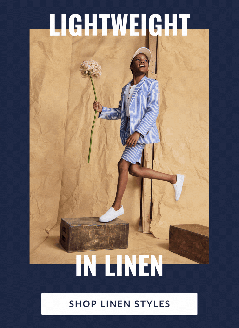 Boy on brown paper background holding flowers wearing blue and white shorts suit with text lightweight in linen and button shop linen styles