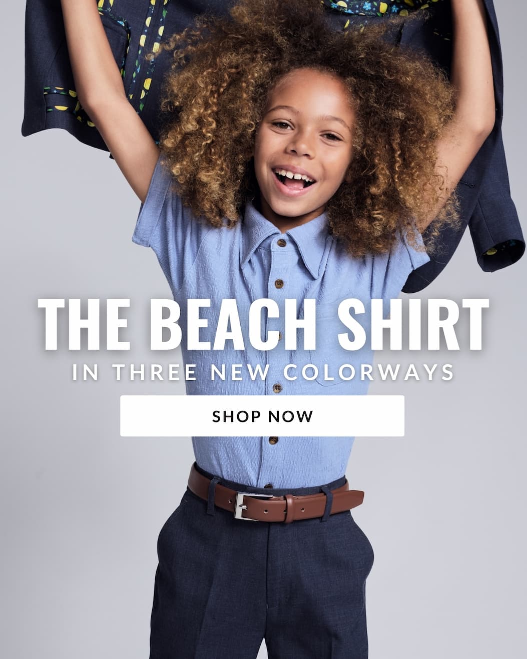 Boy wearing light blue shirt holding suit jacket on grey background with white text the beach shirt now in three colorways and white shop now button